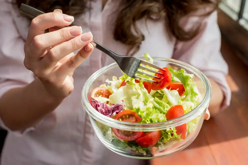 Imagem de uma mulher vestindo roupas de academia segurando um prato com salada e salmão